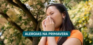 Mulher com sintomas alérgicos assoando o nariz num parque cheio de árvores. Na consta o seguinte texto: Alergias na primavera.